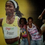 Rosita y Berleidis posan en New Kingston,cerca de una cartelera de Shelly Ann Fraser Pryce, campeona de los 100 metros para mujers de las Olimpiadas de 2008 y 2012